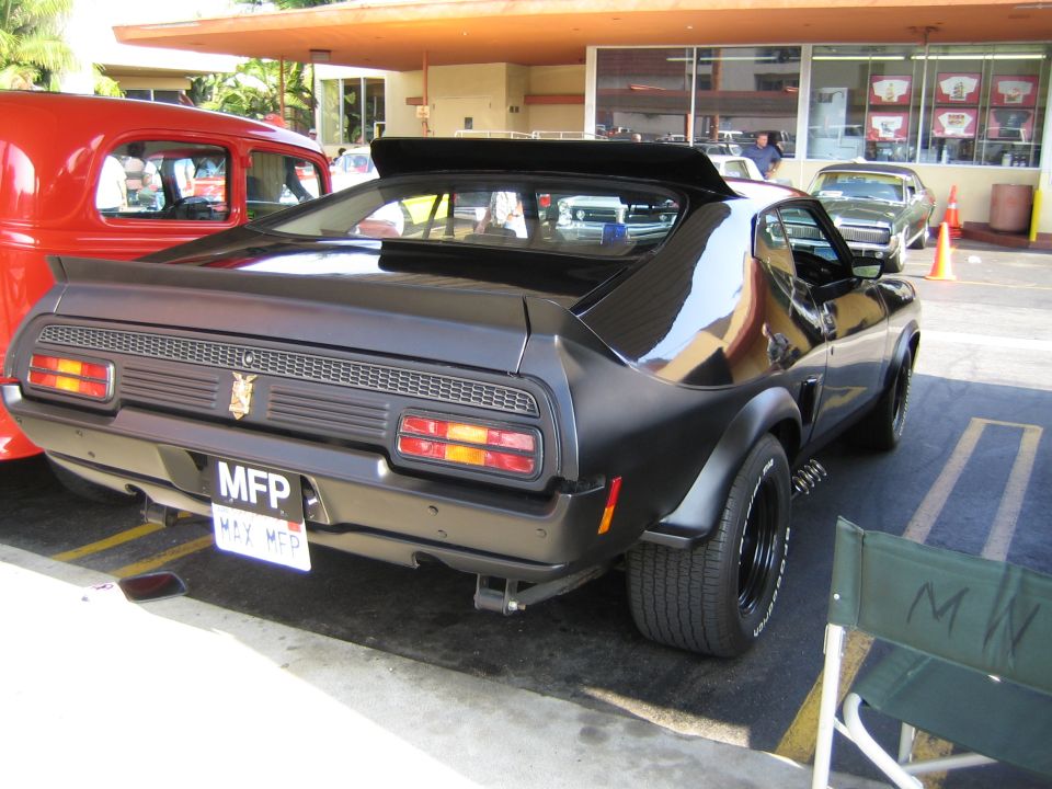 Black coupe with spoiler and custom plate 'MFP MAX MFP'. Red car to the left, other cars in background