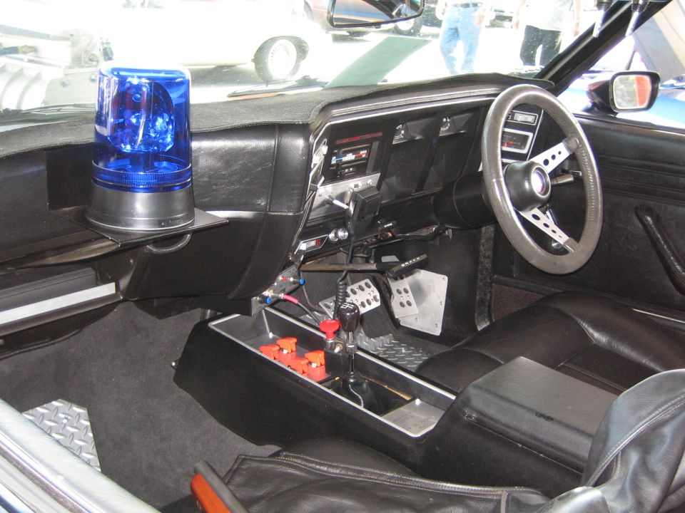1985 Ford Mustang interior, black dashboard with blue light, aftermarket steering wheel, and floor shifter