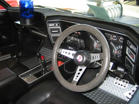 1985 Ford Mustang - The interior of a car features a blue light on the dashboard, an aftermarket steering wheel, and custom floor mats.