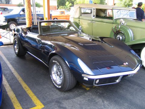 1985 Ford Mustang - A dark blue convertible sports car is parked next to a green vintage car.
