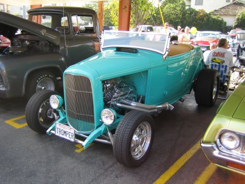 1985 Ford Mustang - A teal hot rod convertible is parked next to a dark-colored truck and a green car.