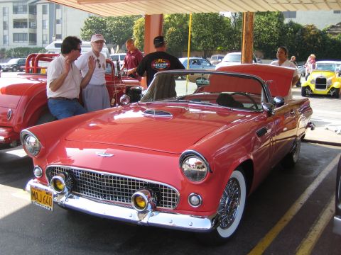 1985 Ford Mustang - A classic red Ford Thunderbird is parked under a canopy, with people gathered around.