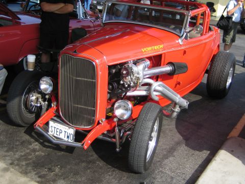 1985 Ford Mustang - A bright red hot rod is parked next to another red car, with its engine and roll cage clearly visible.