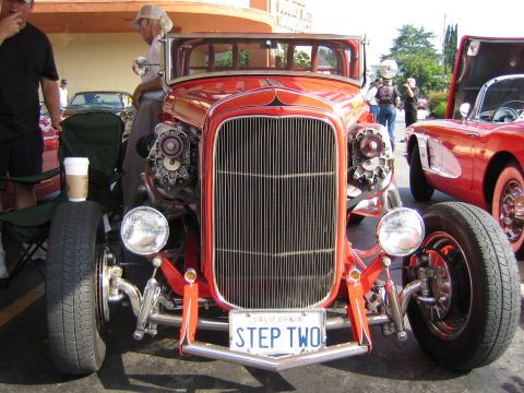 1985 Ford Mustang - A custom red hot rod is displayed next to a red Corvette at an outdoor event.