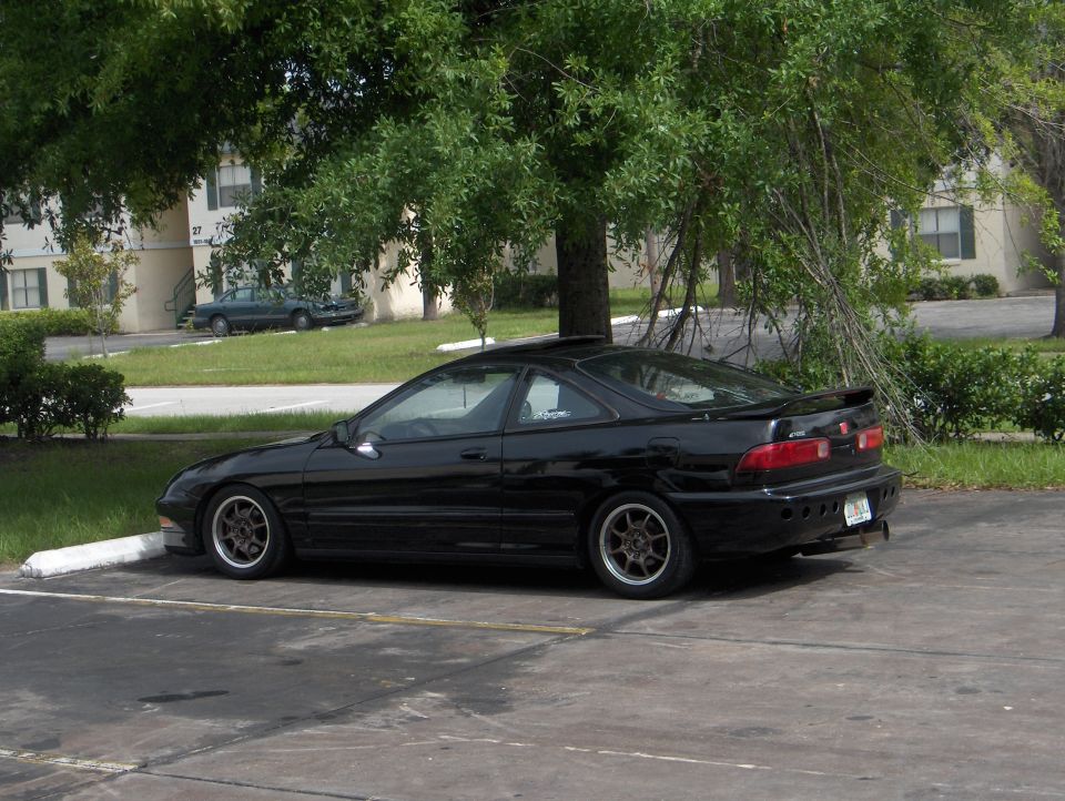 Black Acura Integra coupe, rear-side view, with bronze wheels parked in a lot