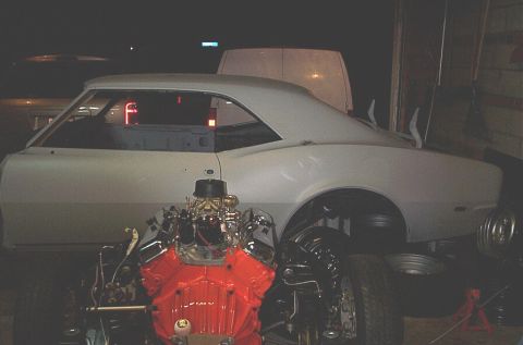 1968 Chevrolet Camaro - A classic car body is prepped for restoration, with a powerful V8 engine positioned in front of it.