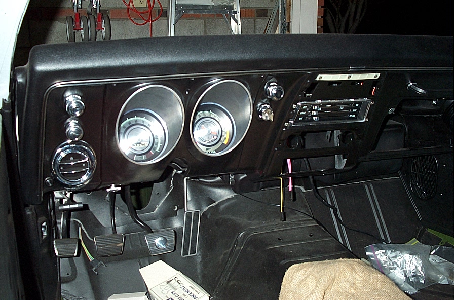 Black 1st-gen Camaro dashboard under restoration with gauges, bare floor and pedals