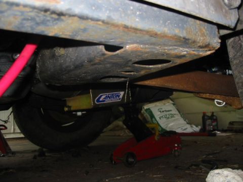1985 Ford LTD Crown Victoria - Underbody view of a vehicle, a Canton brace and a tire, with a red jack and soil bags visible.