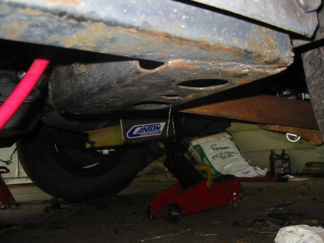 Underbody view showing a Canton brace and a tire, with a red jack and bags of soil in the background
