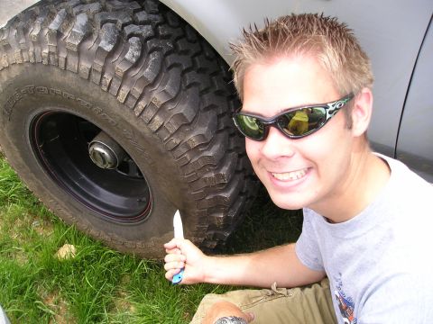 1996 Ford Bronco - A man poses with a knife next to the large tire of a 1996 Ford Bronco.