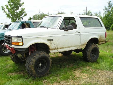 1996 Ford Bronco - A muddy white Ford Bronco sits in a grassy field next to another vehicle.