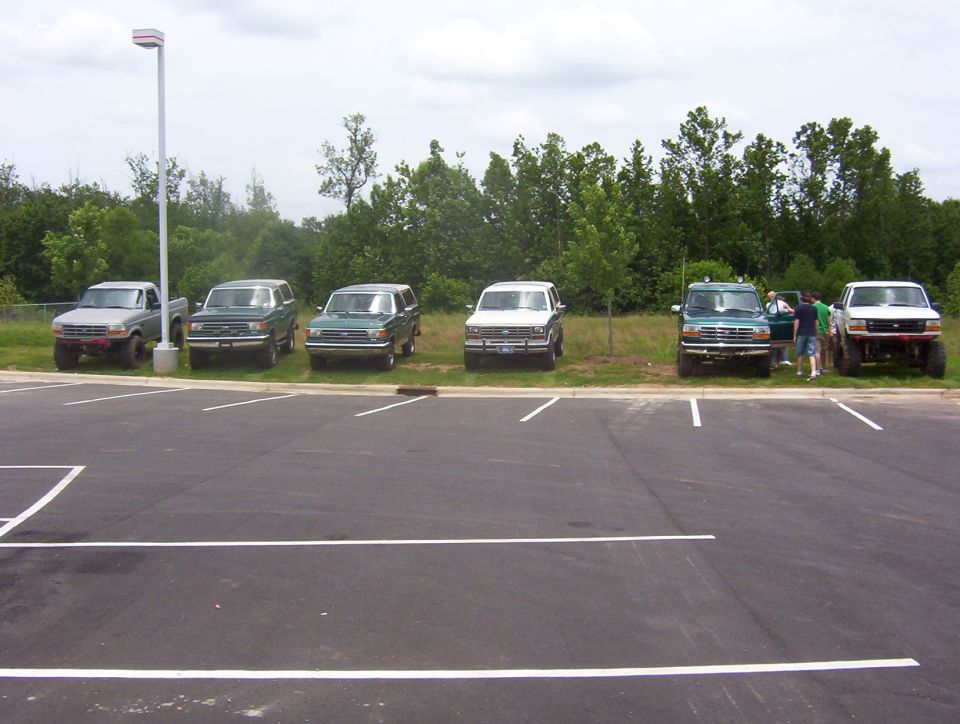 Several SUVs and a pickup truck are parked in a lot near trees