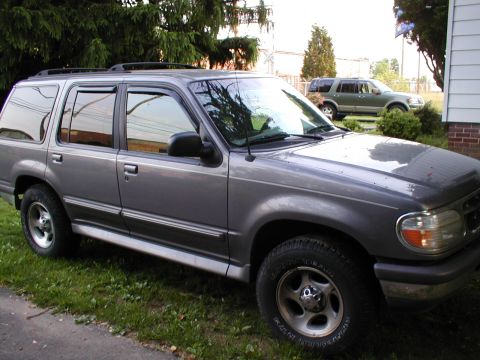 1979 Ford Bronco - A gray Ford Explorer is parked in a grassy area next to a house, with another SUV visible in the background.