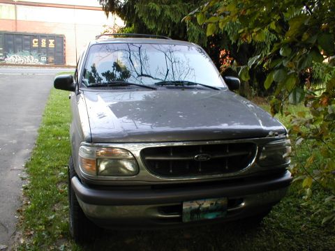 1979 Ford Bronco - This gray Ford Explorer SUV is parked on the side of a road, partially obscured by trees.