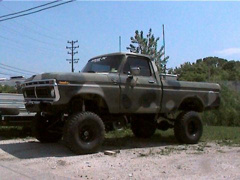 1977 Ford F-150 - A lifted 1970s Ford F-150 regular cab pickup in green and black camouflage paint, shown from a 3/4 front angle on oversized off-road tires…