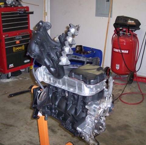 1999 Mitsubishi Mirage - Engine assembly sits on a stand in a garage, ready for installation or further work.