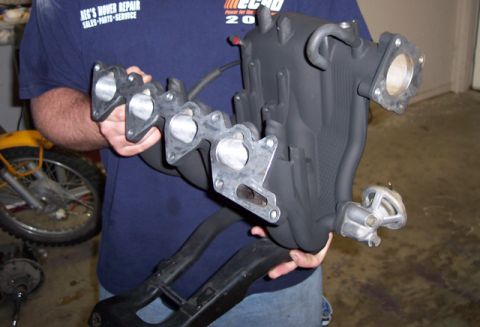 1999 Mitsubishi Mirage - A person holds a black intake manifold, with a yellow motorcycle visible in the background.