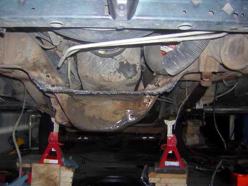 Vehicle undercarriage on red jack stands showing rusty differential, driveshaft and exhaust.