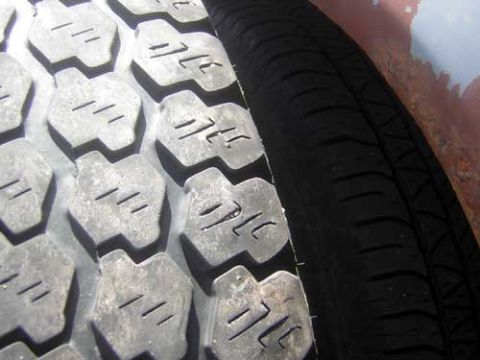 1986 Ford Bronco II - A close-up view of a tire's tread pattern and sidewall, with a rusty surface in the background.