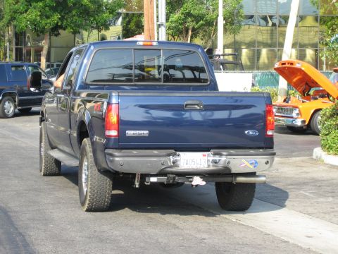 1985 Ford Mustang - A blue Ford F-Series truck is parked on the street, with an orange classic car visible in the background.