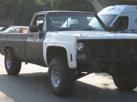 1985 Ford Mustang - A two-tone pickup truck, appearing to be a Chevrolet C/K series from the late 1970s or early 1980s, is shown with large off-road tires.
