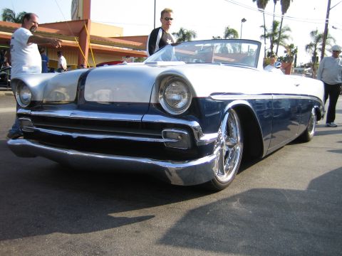 1985 Ford Mustang - Low front three-quarter shot of a slammed mid-1950s American convertible custom in two-tone white over dark blue, with a shaved smooth hood…