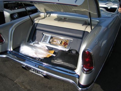 1985 Ford Mustang - The trunk of a classic Chevrolet reveals custom audio equipment and a black leather bag, with another car visible in the background.