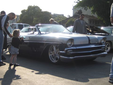 1985 Ford Mustang - A two-tone convertible with chrome wheels and a lowered stance is parked outdoors with people around.