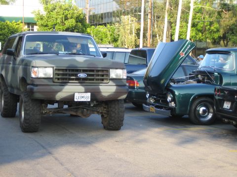 1985 Ford Mustang - Camouflaged Ford Bronco SUV parked next to other vehicles, one with its hood open.