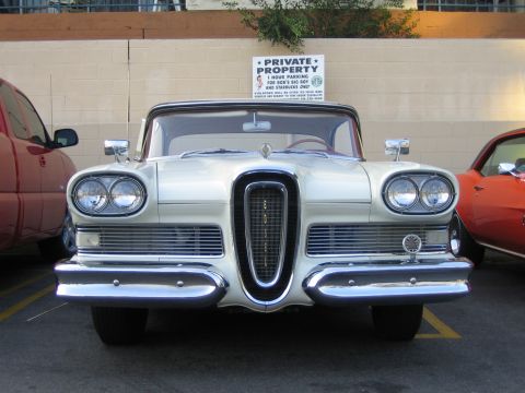 1985 Ford Mustang - A white 1958 Edsel Pacer is parked in front of a brick wall, with other vehicles nearby.