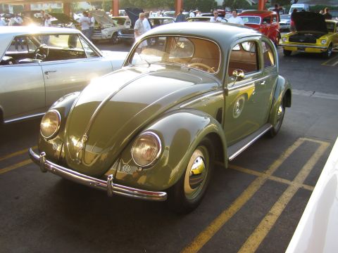 1985 Ford Mustang - A classic green Volkswagen Beetle is parked in a lot with other vehicles.
