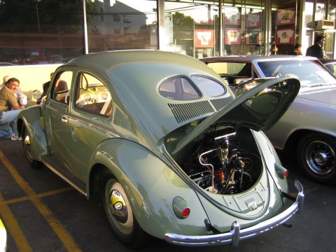 1985 Ford Mustang - Light green Volkswagen Beetle with rear engine compartment open, parked next to a silver car.