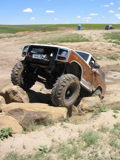 1981 Ford Bronco - This heavily modified SUV is navigating a challenging rocky terrain with its front wheels elevated.