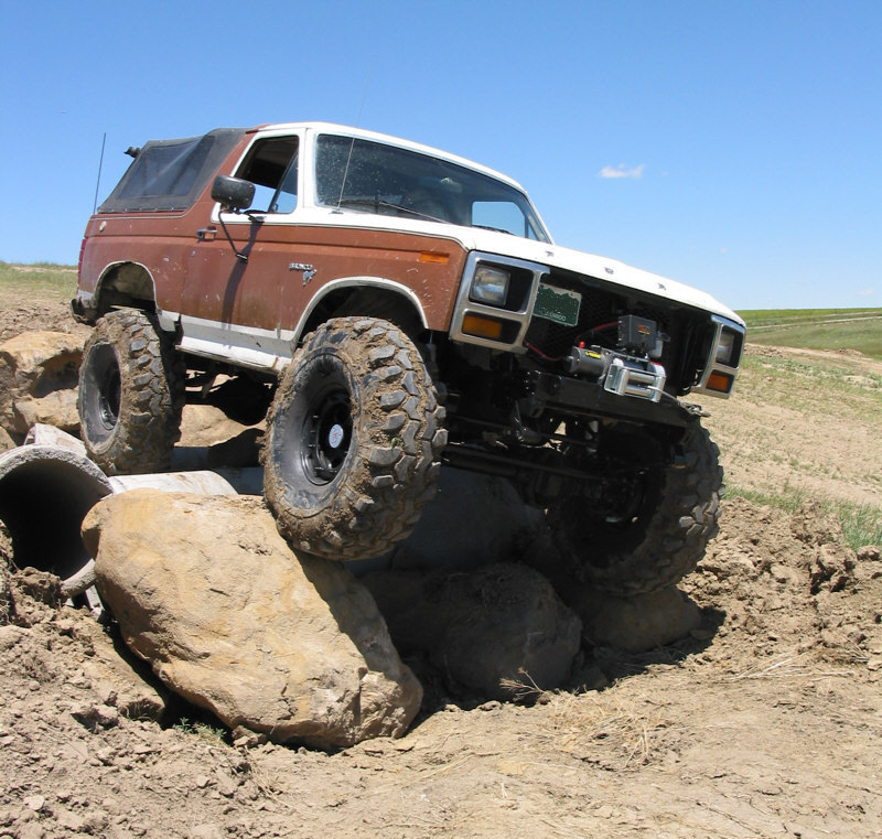 Lifted brown and white Ford Bronco with winch crawling over boulders on dirt