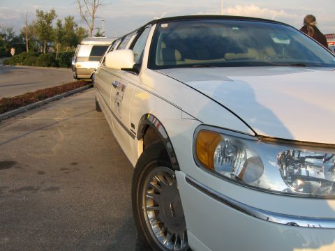 1992 Ford Crown Victoria - A white limousine is parked next to a white van on a paved lot.
