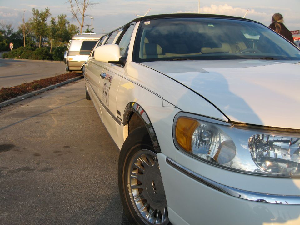 White limousine front quarter view with a white van in the background