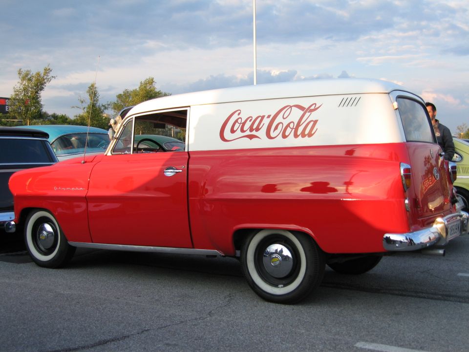 Red and white Coca-Cola delivery van parked on asphalt, other vehicles visible in background