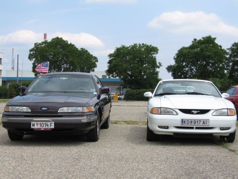 1992 Ford Crown Victoria - Two cars, a dark sedan and a white coupe, are parked next to each other, both facing forward. The sedan displays a license plate reading "W…