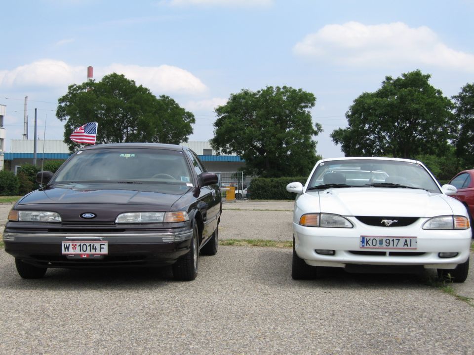 Dark sedan and white coupe parked side-by-side, front view. The sedan has a "W 1014 F" license plate