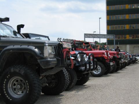 1992 Ford Crown Victoria - A line of off-road vehicles, including a black Jeep Cherokee and several red Jeep Wranglers, are parked in a lot.