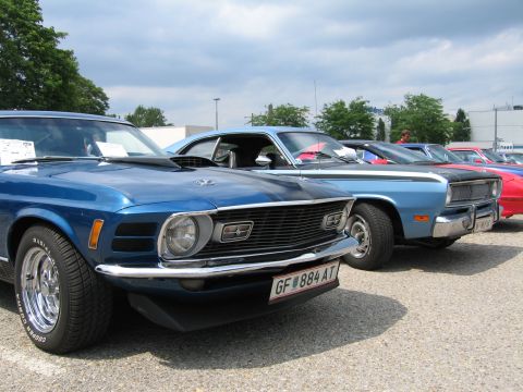 1992 Ford Crown Victoria - A line of classic cars, including a blue 1970 Ford Mustang Mach 1, are parked outdoors under a cloudy sky.
