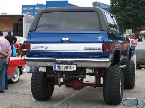 1992 Ford Crown Victoria - A lifted blue Chevrolet K5 Blazer with custom decals and large off-road tires is seen from the rear, parked next to a red car.