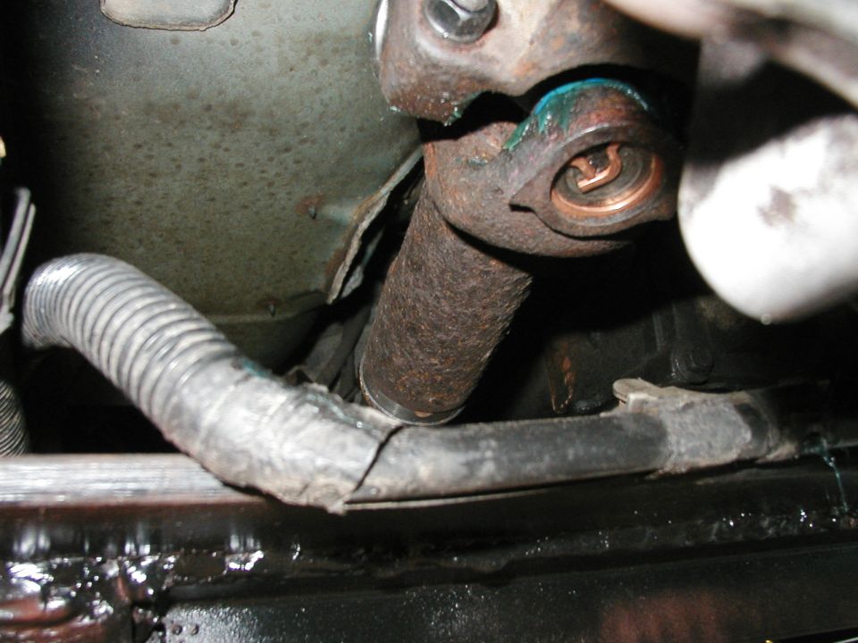 Close-up of a rusty driveshaft U-joint with a torn protective boot and wiring