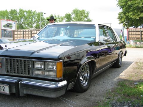 1992 Ford Crown Victoria - This black sedan features a white roof and chrome wheels, with a person visible inside.