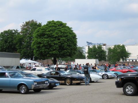 1992 Ford Crown Victoria - A variety of vehicles are parked at an outdoor event, with a blue classic car and a black pickup truck prominently visible.