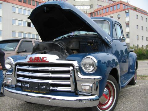 1992 Ford Crown Victoria - A classic blue GMC pickup truck is displayed with its hood open, parked next to a modern SUV.