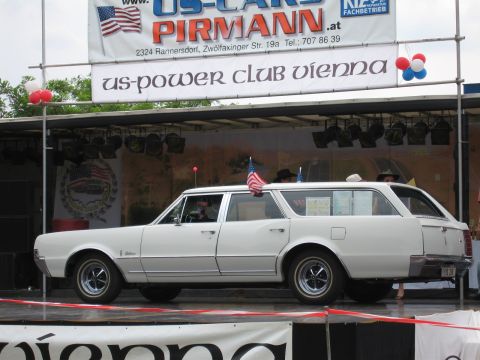 1992 Ford Crown Victoria - A white station wagon is displayed on a stage with a banner for US-Cars Pirman and US-Power Club Vienna.