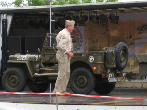 1992 Ford Crown Victoria - A man in a military uniform stands beside a vintage green jeep with a spare tire mounted on the rear.