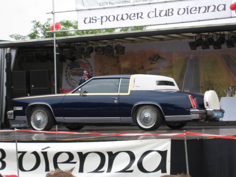 1992 Ford Crown Victoria - A dark blue coupe with a white vinyl roof and a continental kit is displayed on a stage.