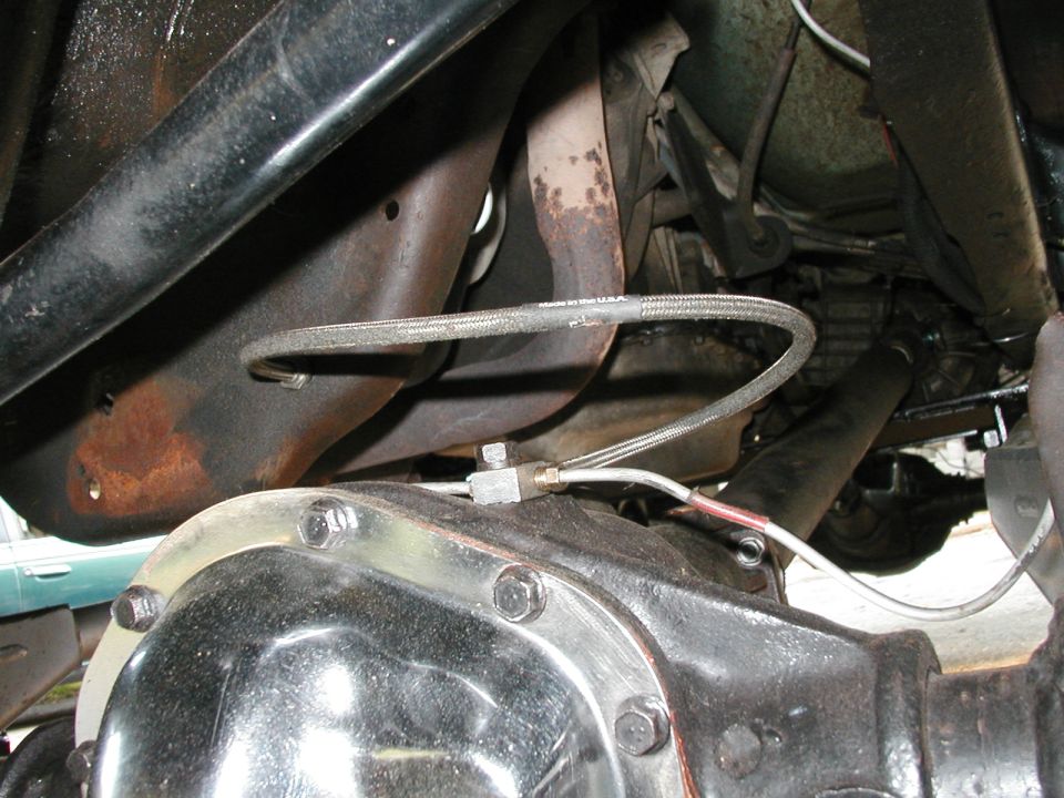 Undercarriage view of a vehicle's rear differential and exhaust system. A braided metal brake line is visible